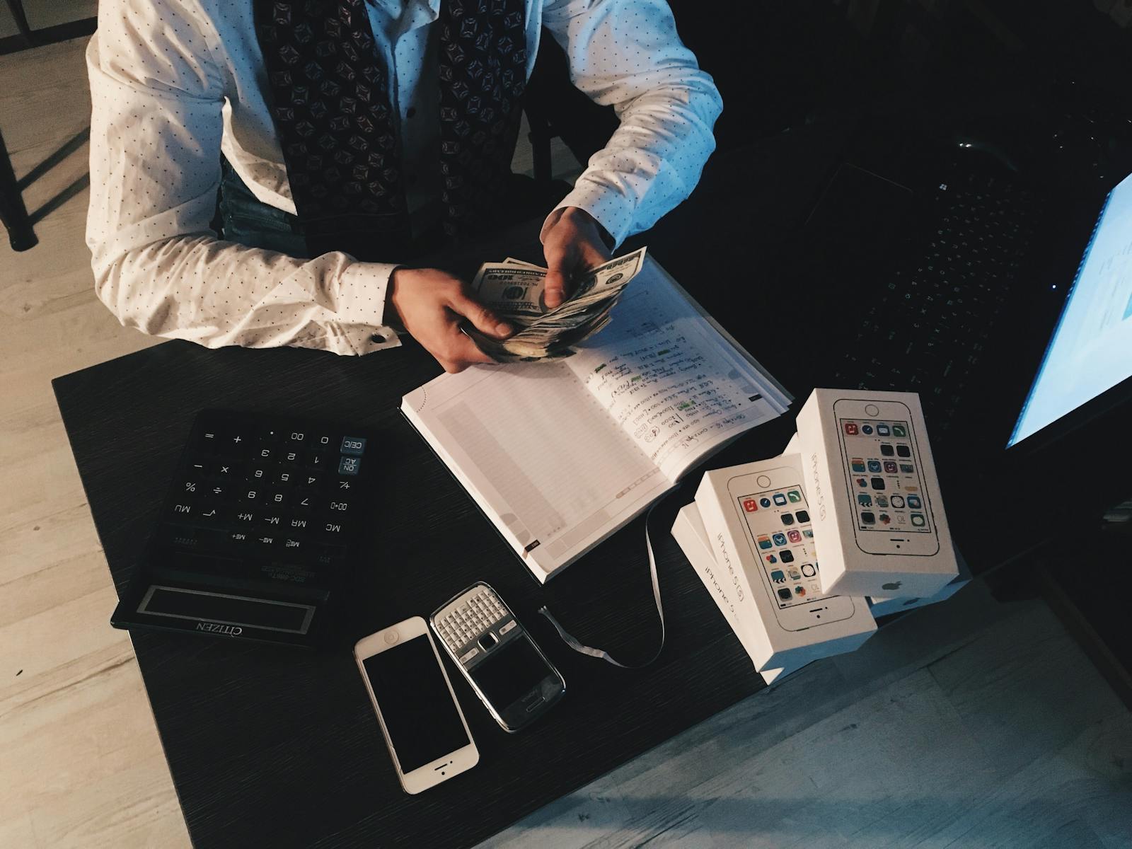 Man counting money at a desk with smartphones, calculator, and notebook.