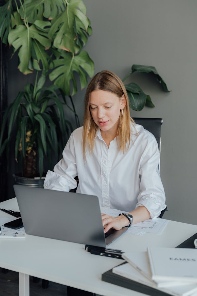 Person working on a laptop at a desk with green plants in a modern office setting