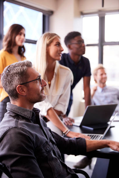 Group of diverse colleagues collaborating at a business meeting with laptops in a modern office setting