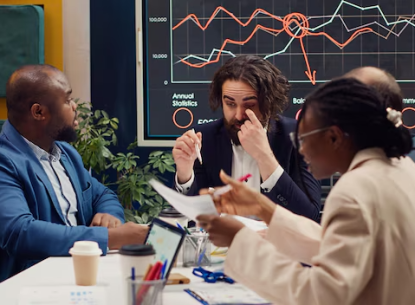 Business team discussing a financial graph in a meeting room with charts displayed on a screen in the background